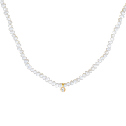 A white freshwater pearl necklace with a small gold pendant featuring a clear round-cut topaz gemstone, displayed against a solid white background.