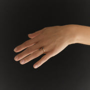 A hand wearing a delicate gold ring with small dark faceted diamonds, posed against a solid black background.