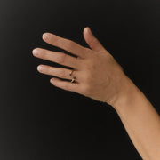 A hand wearing a delicate gold ring with small dark faceted diamonds, posed against a solid black background.
