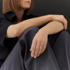 A close-up lifestyle shot of a model wearing a gold & grey diamonds ring with a vertical black inlay, sitting in a dark navy shirt and trousers against a dark gray background.