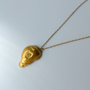 Gold leaf-shaped pendant on a chain against a light gray background