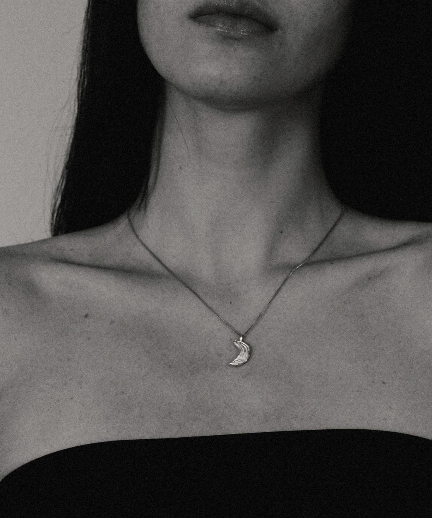 Close-up of a person wearing a necklace with a moon pendant.