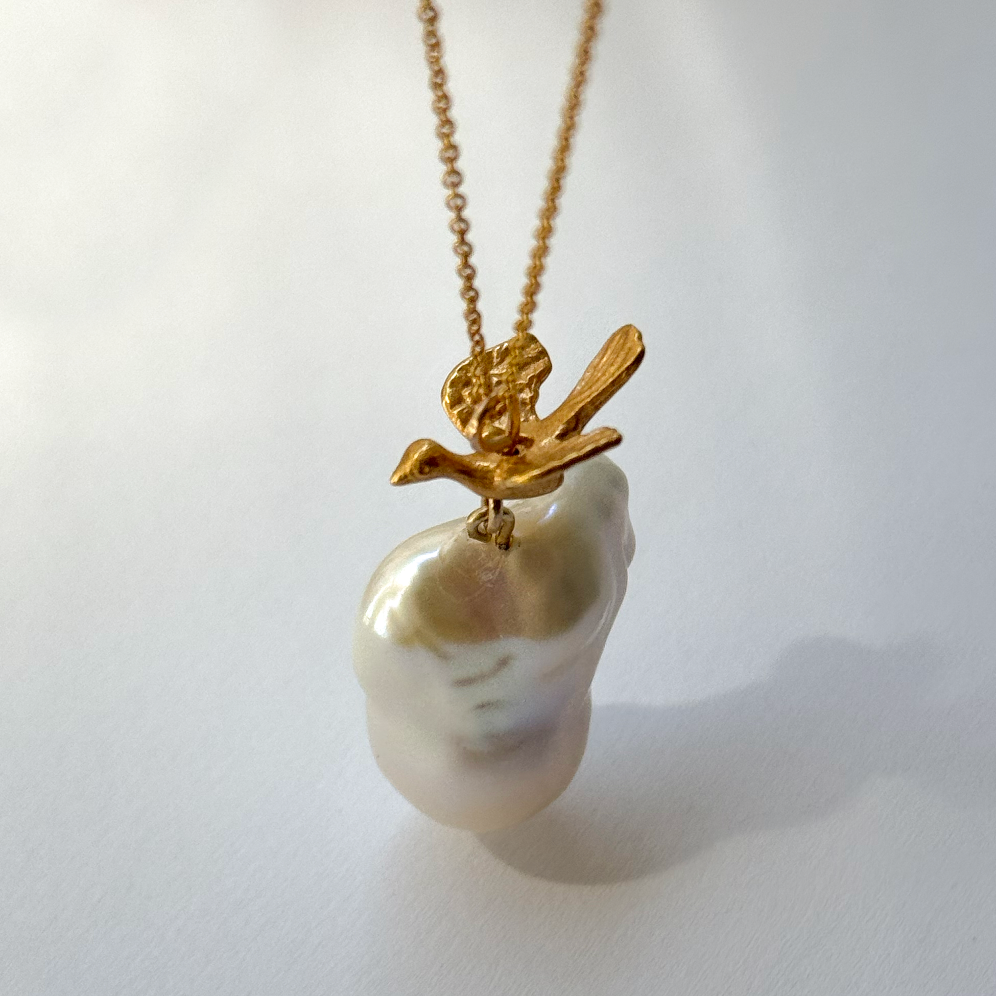 Gold-plated silver bird pendant accompanied by a baroque-shaped freshwater pearl. 