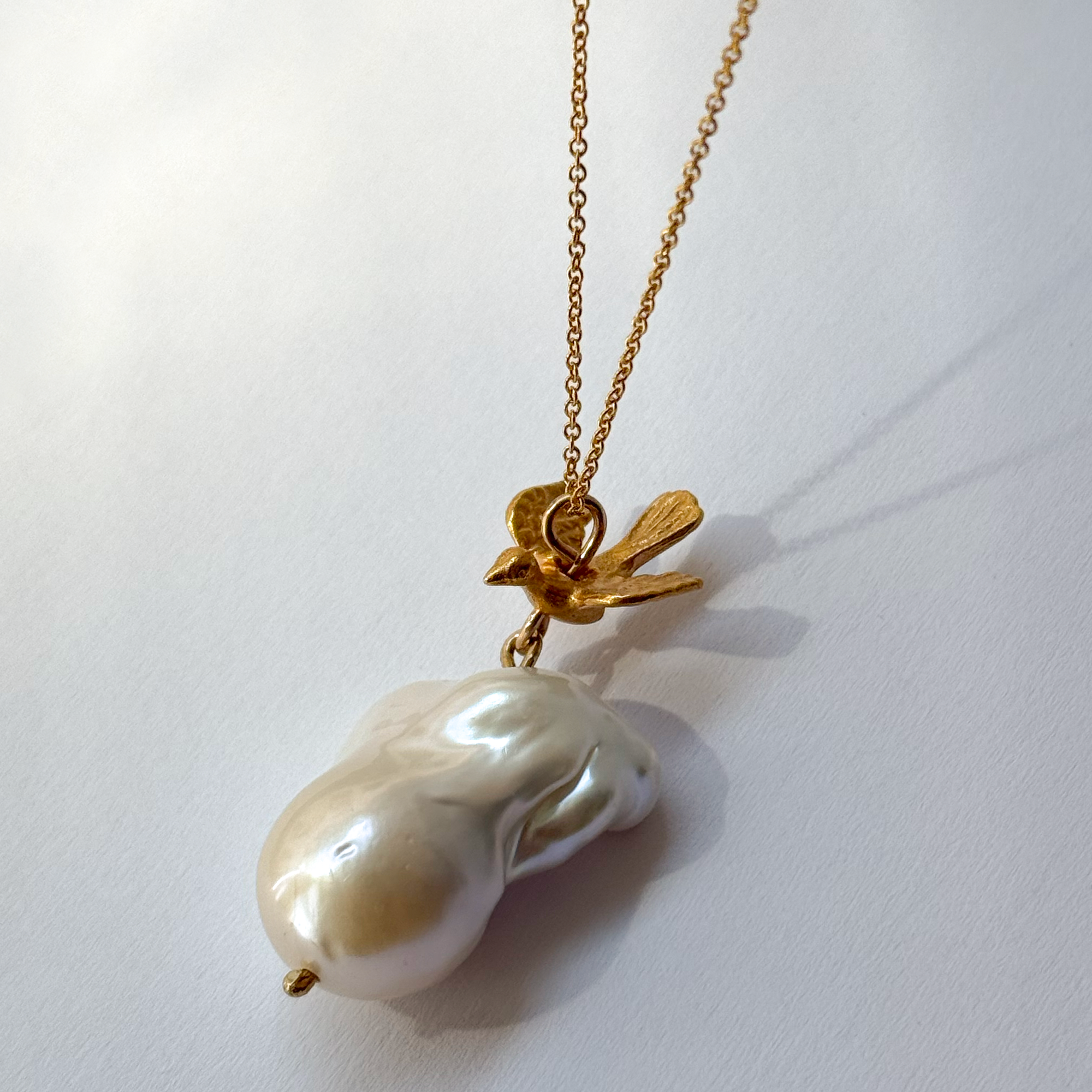 Gold-plated silver bird pendant accompanied by a baroque-shaped freshwater pearl. 