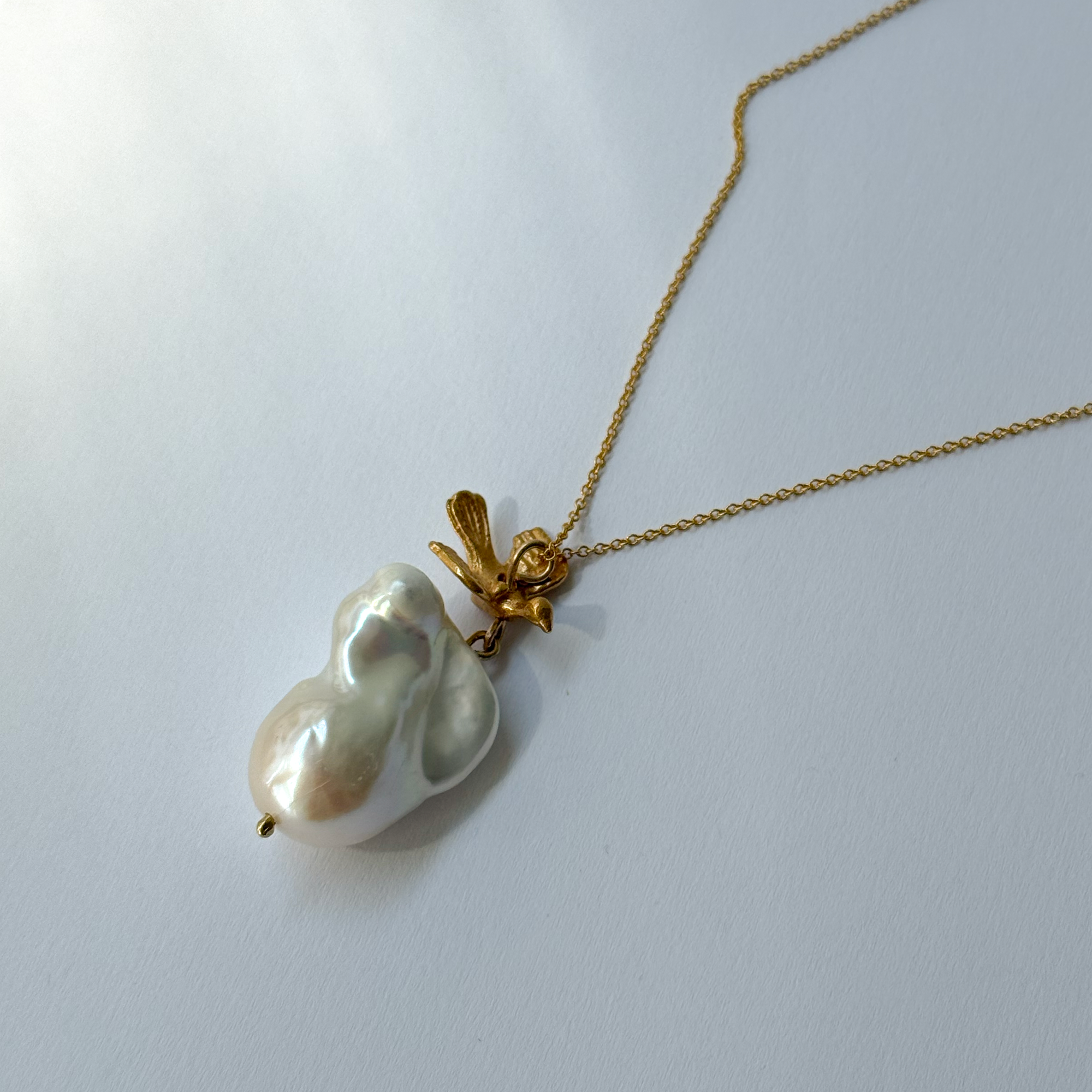 Gold-plated silver bird pendant accompanied by a baroque-shaped freshwater pearl. 