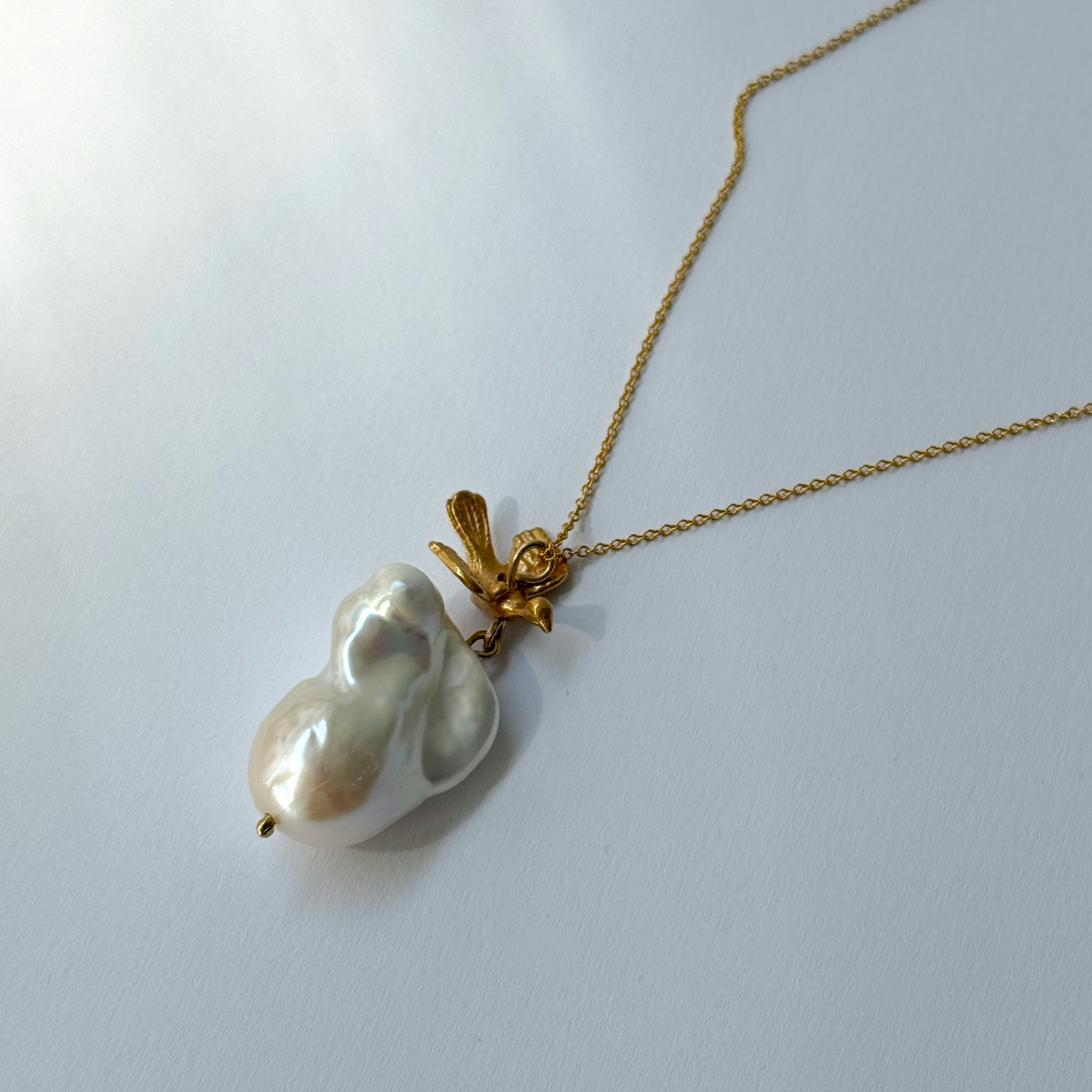 Gold-plated silver bird pendant accompanied by a baroque-shaped freshwater pearl. 