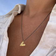 A person wearing a gold plated heart-shaped necklace with an oxidized silver chain.