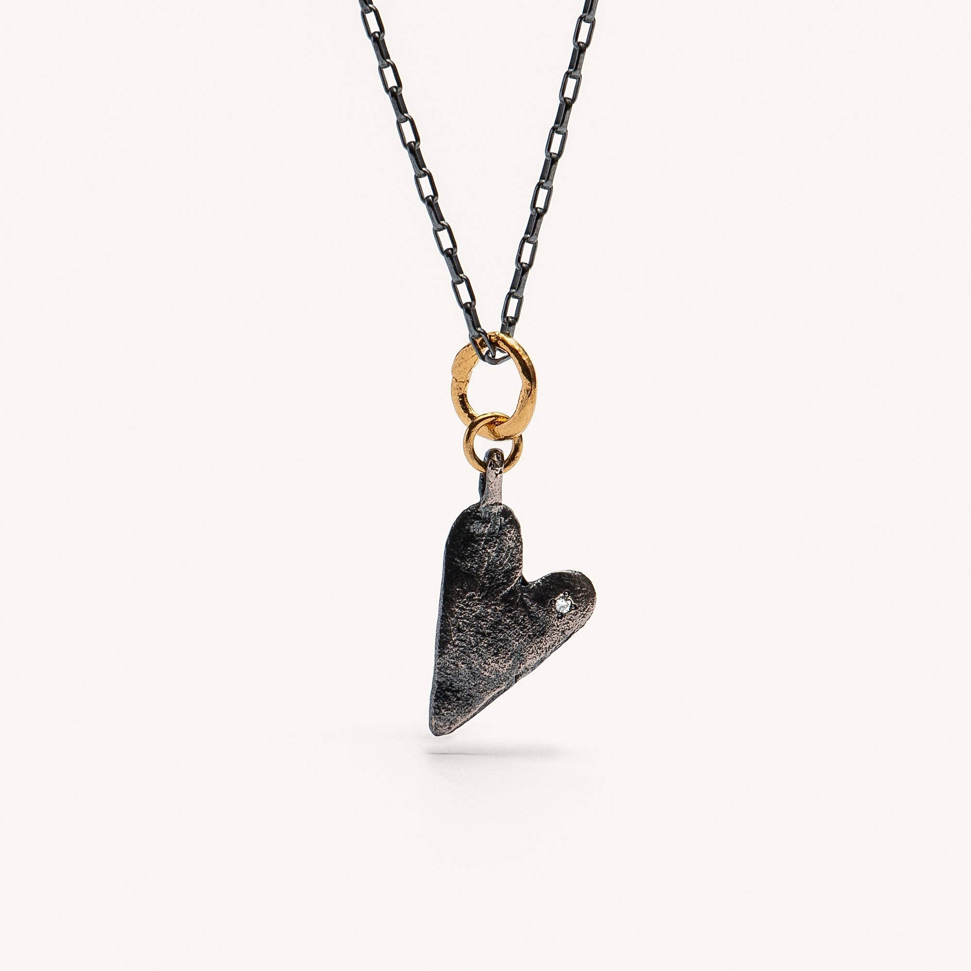 A heart-shaped gold plated silver necklace with a chain and a small white diamond attached to the heart-shaped pendant.
