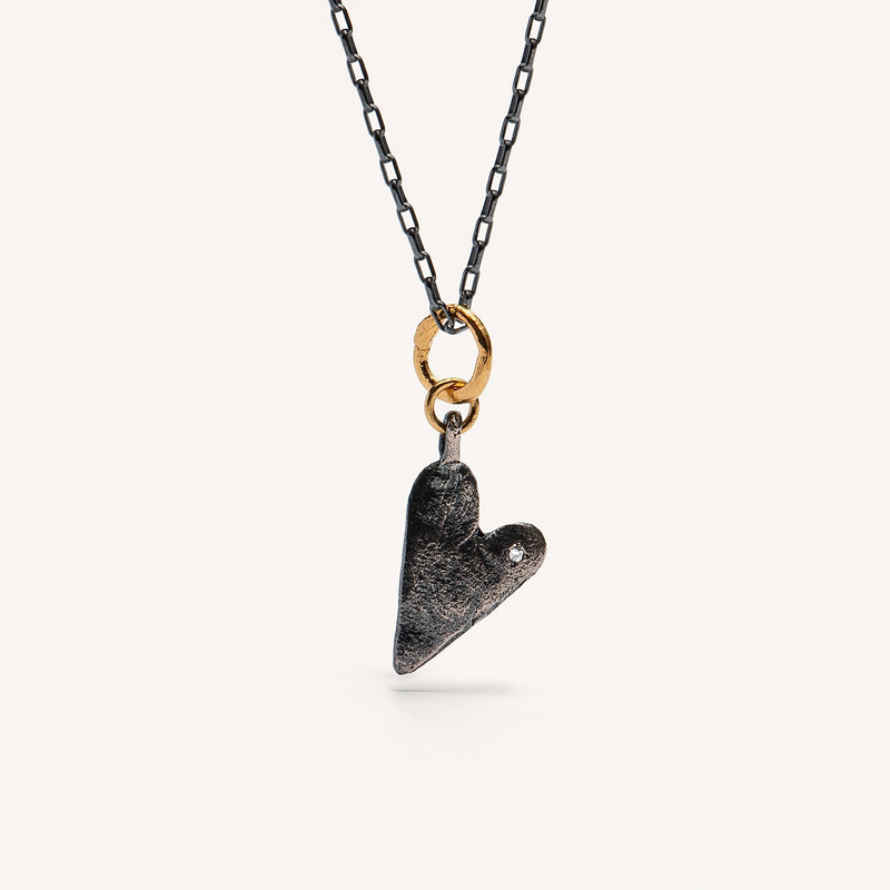 A heart-shaped gold plated silver necklace with a chain and a small white diamond attached to the heart-shaped pendant.