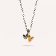 A gold-plated oxidized silver necklace with two heart-shaped silver pendants, one with a pink sapphire center.