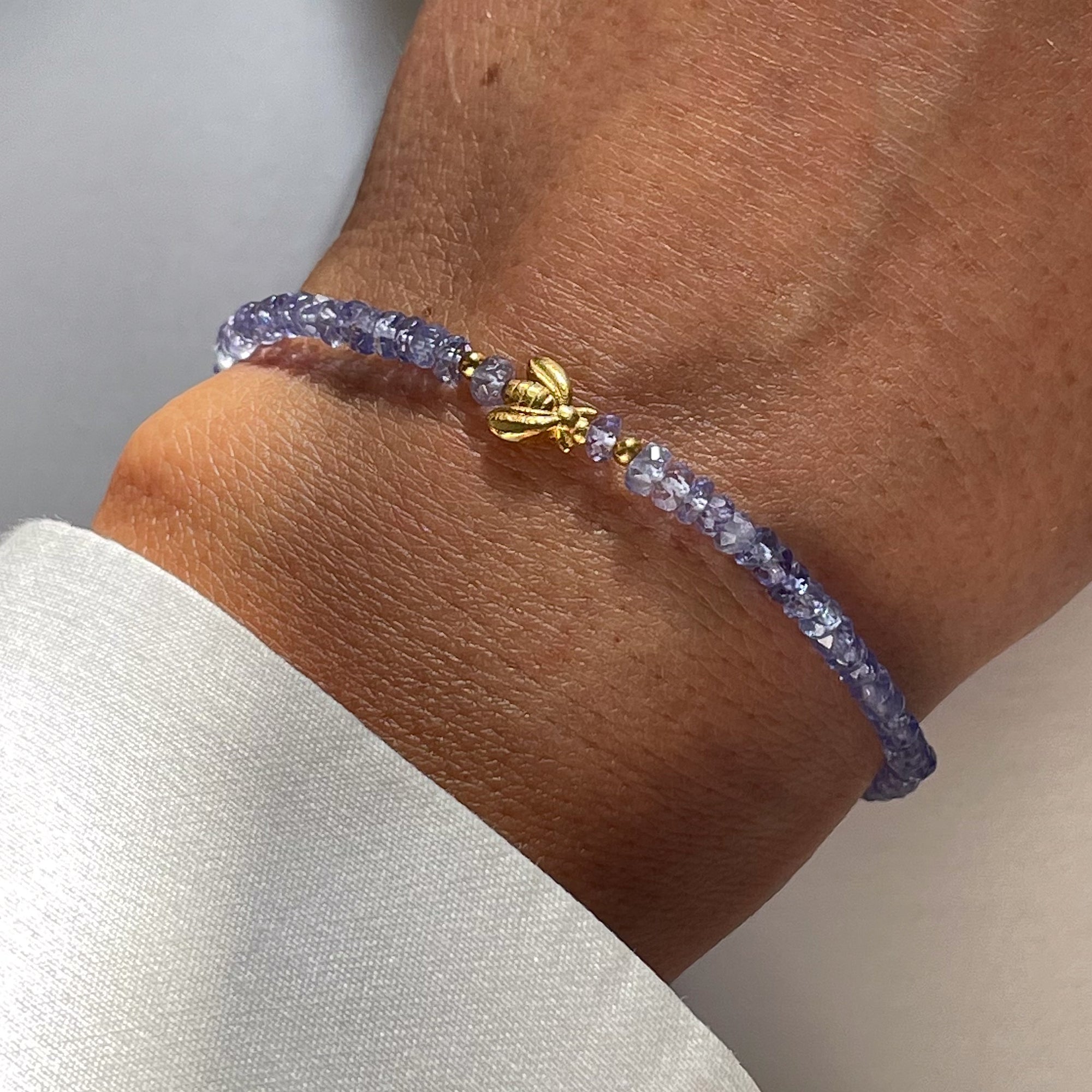 A gold-plated silver bracelet with tanzanite beads and a gold-plated bee-shaped pendant on a person's wrist.