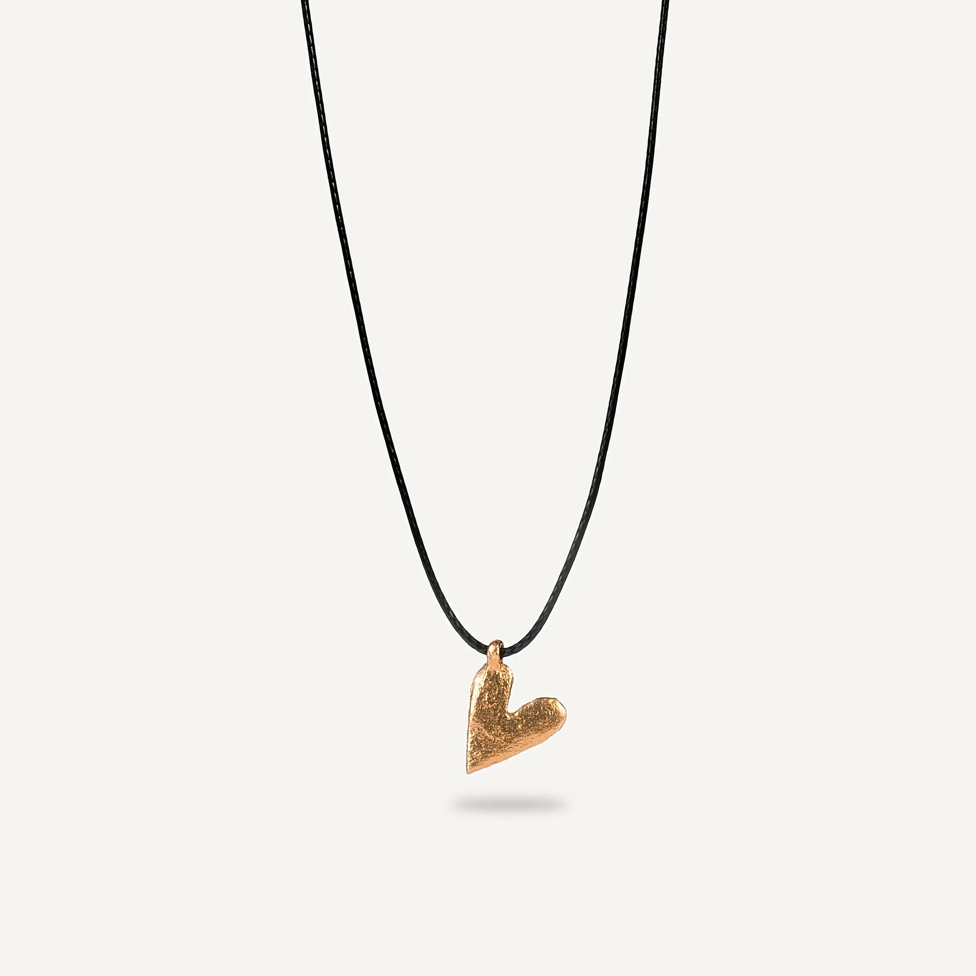A gold plated silver necklace with a heart-shaped pendant on a black string.