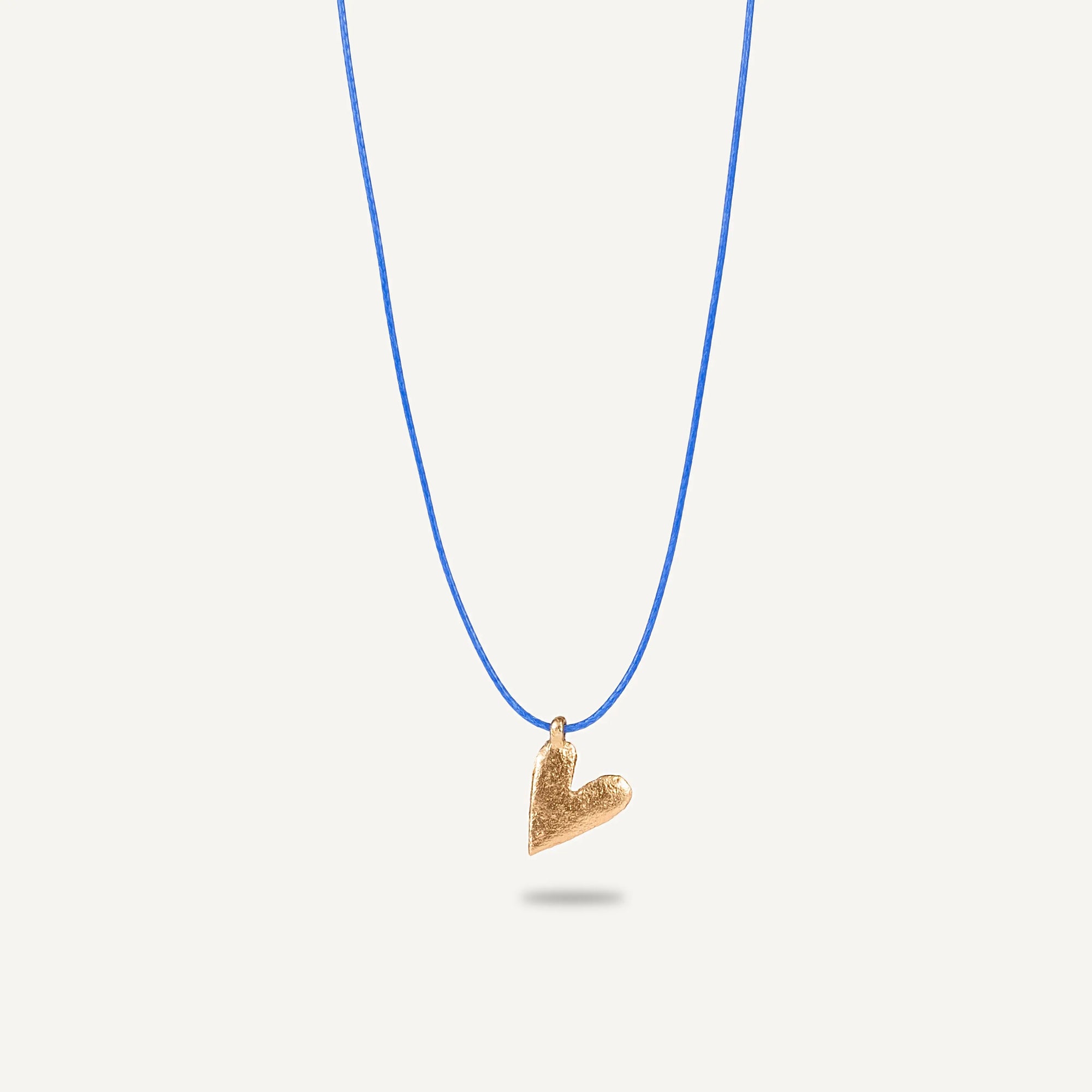 A gold plated silver necklace with a heart-shaped pendant on a blue string.