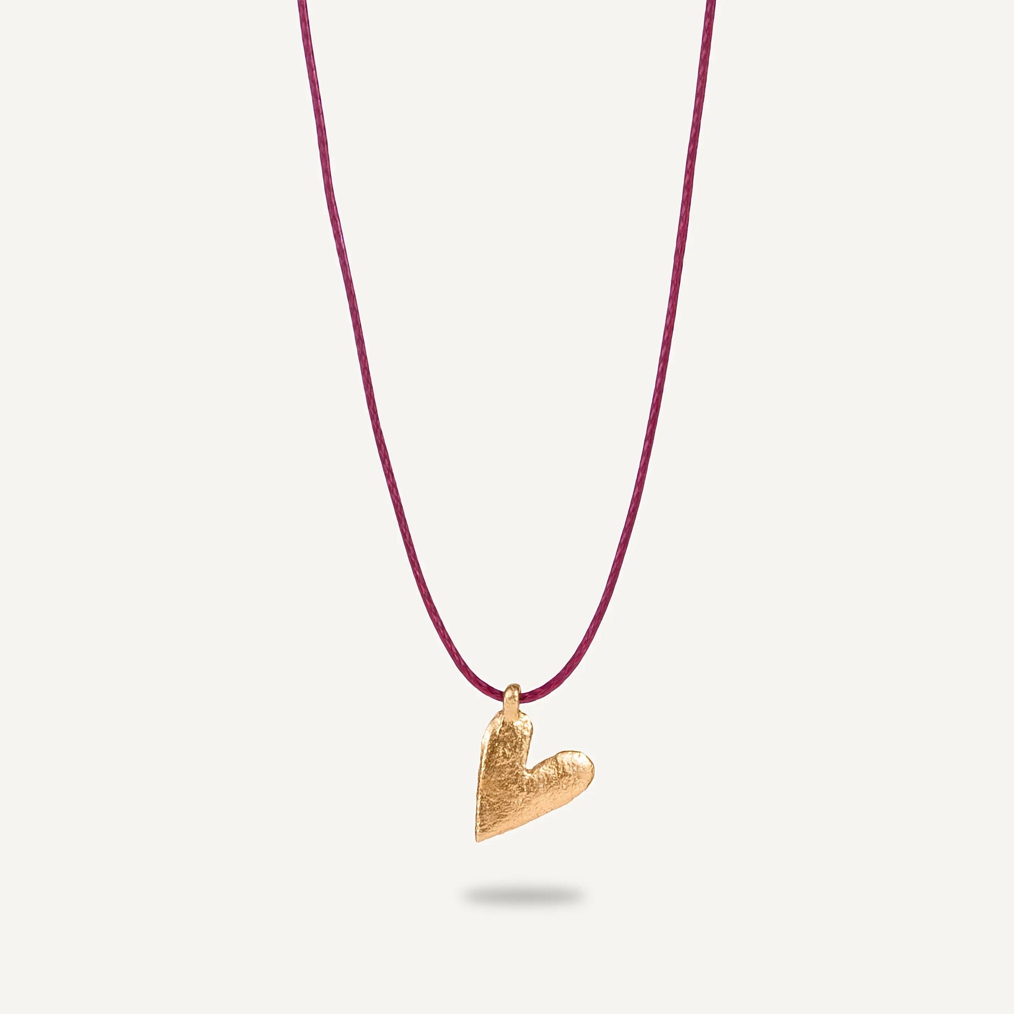 A gold plated silver necklace with a heart-shaped pendant on a burgundy string.