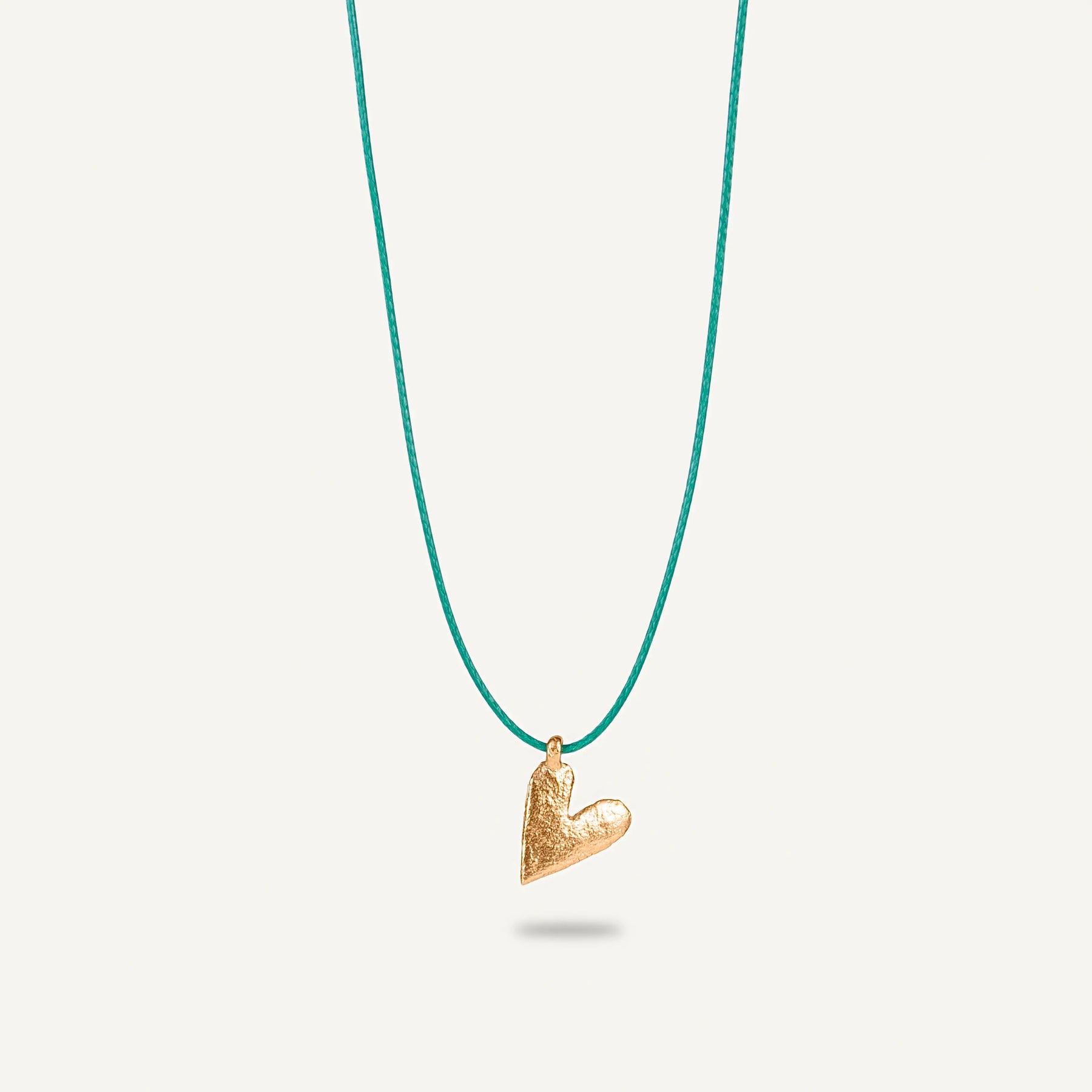 A gold plated silver necklace with a heart-shaped pendant on a green string.