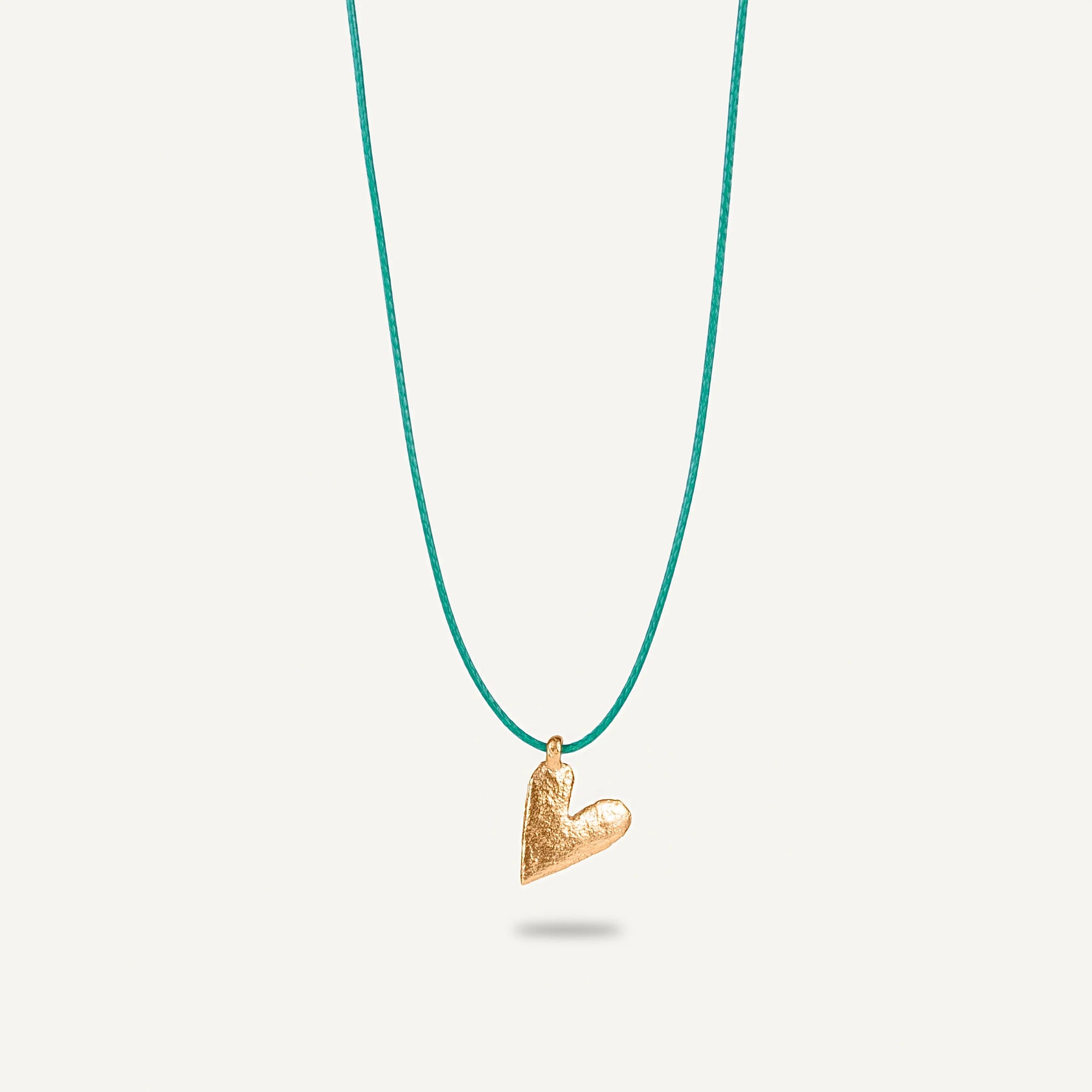 A gold plated silver necklace with a heart-shaped pendant on a green string.