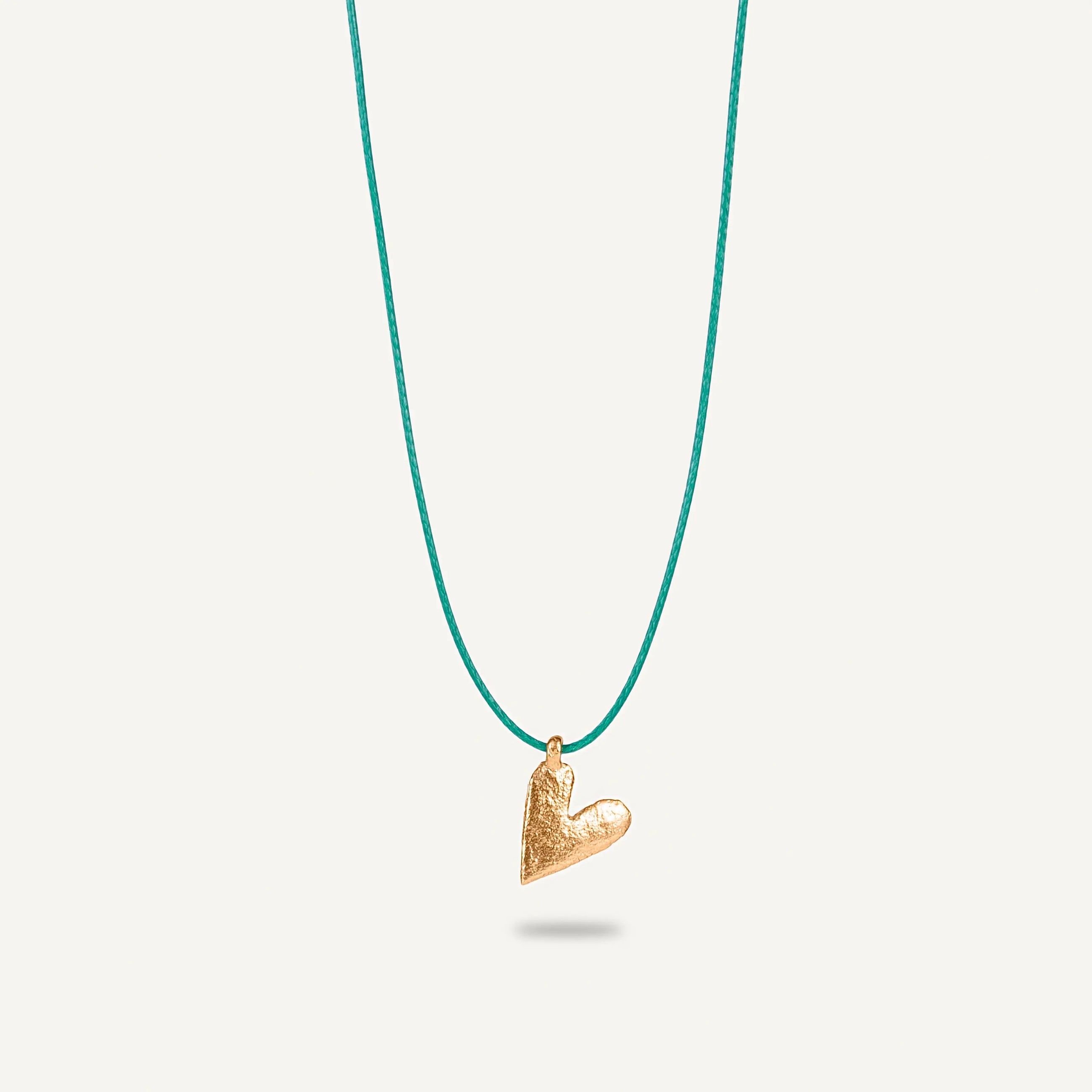 A gold plated silver necklace with a heart-shaped pendant on a green string.