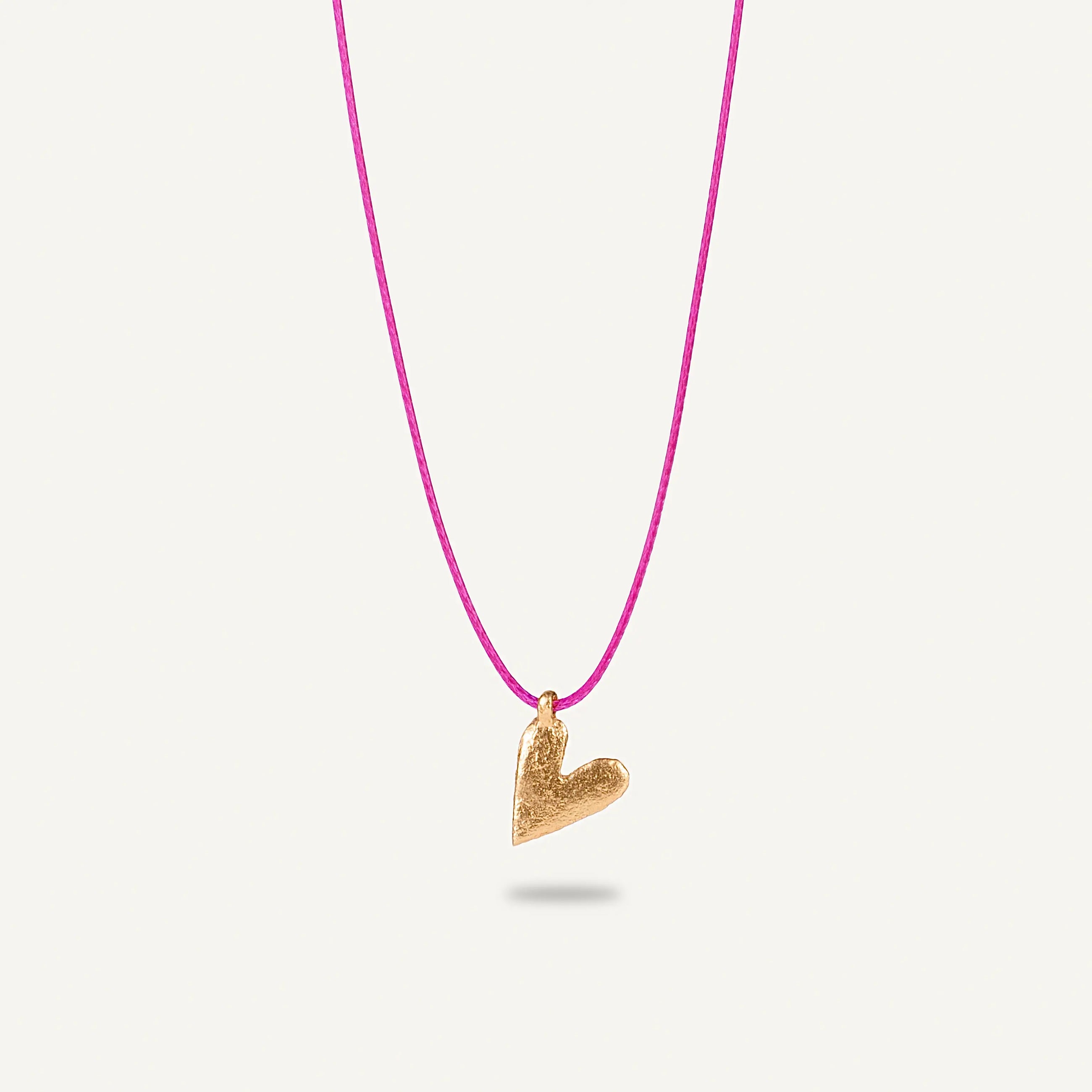 A gold plated silver necklace with a heart-shaped pendant on a pink string.