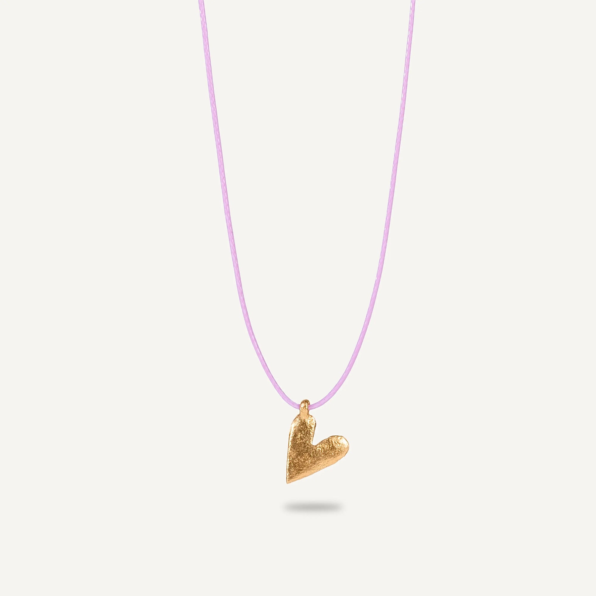 A gold plated silver necklace with a heart-shaped pendant on a purple string.