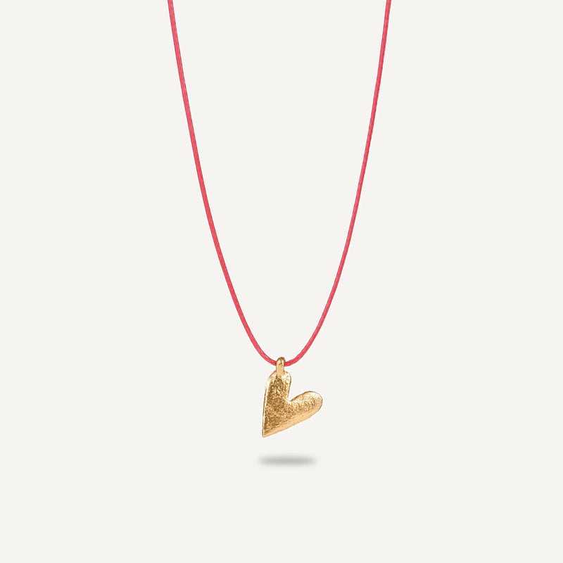 A gold plated silver necklace with a heart-shaped pendant on a red string.