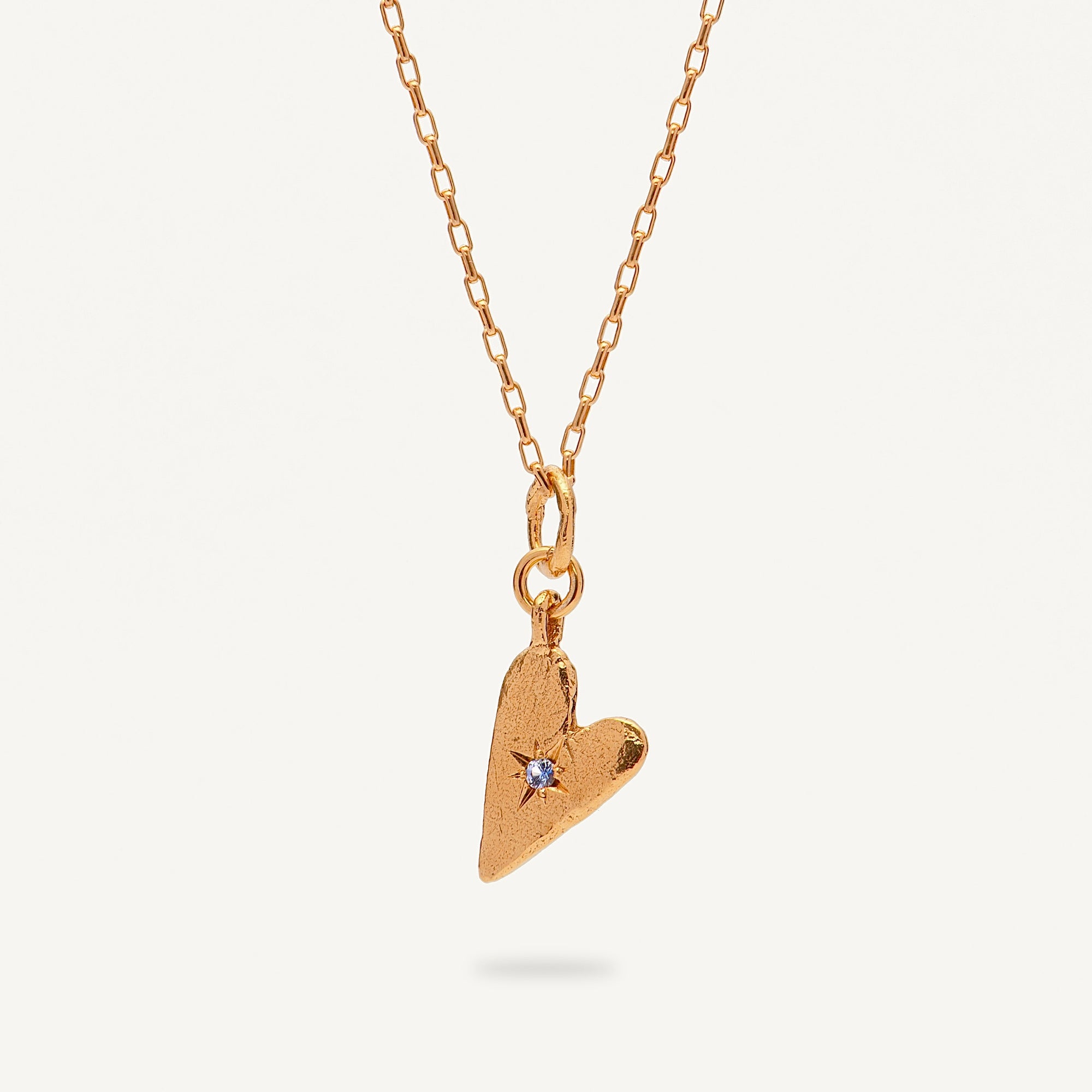 Gold heart-shaped pendant necklace with a small blue gemstone on a white background