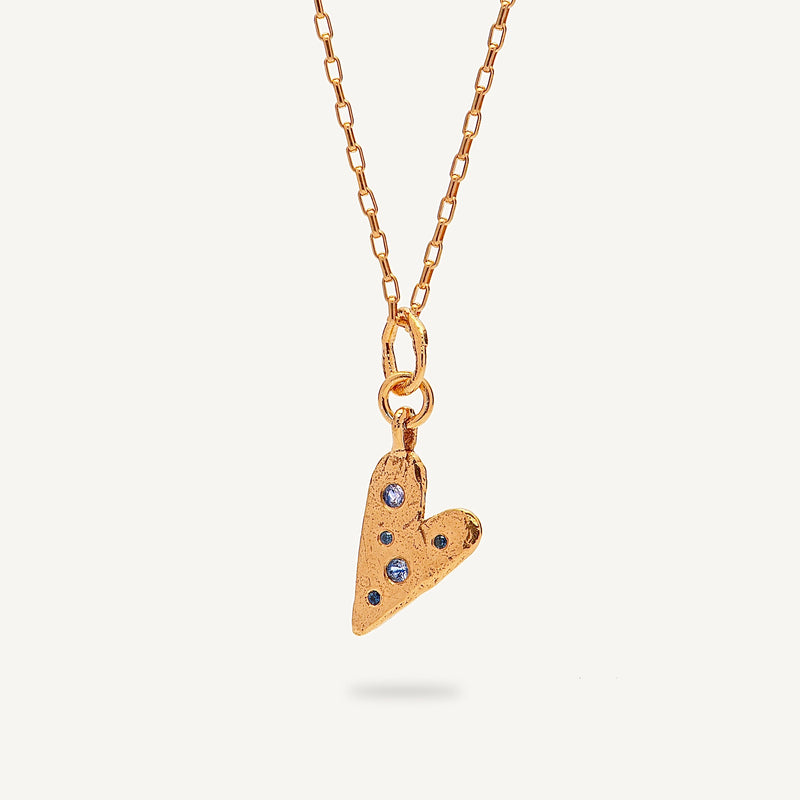 Gold heart-shaped pendant necklace with embedded stones on a light beige background