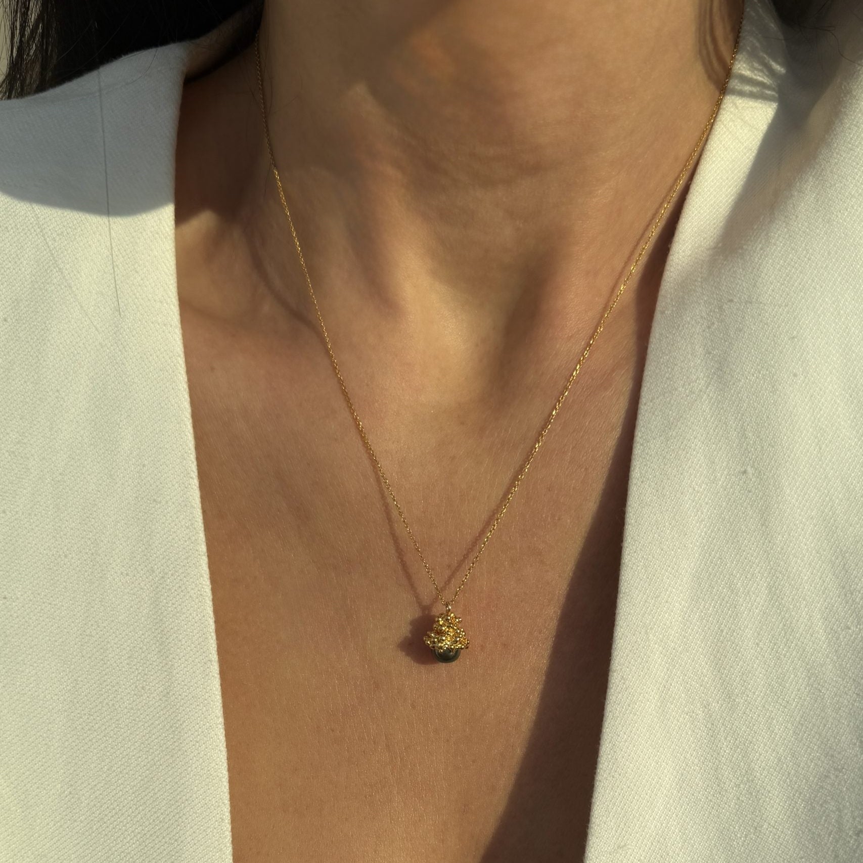 Gold-plated silver pendant with dark pearl by Near Me on a persons neck.