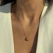 Gold-plated silver pendant with dark pearl by Near Me on a persons neck.