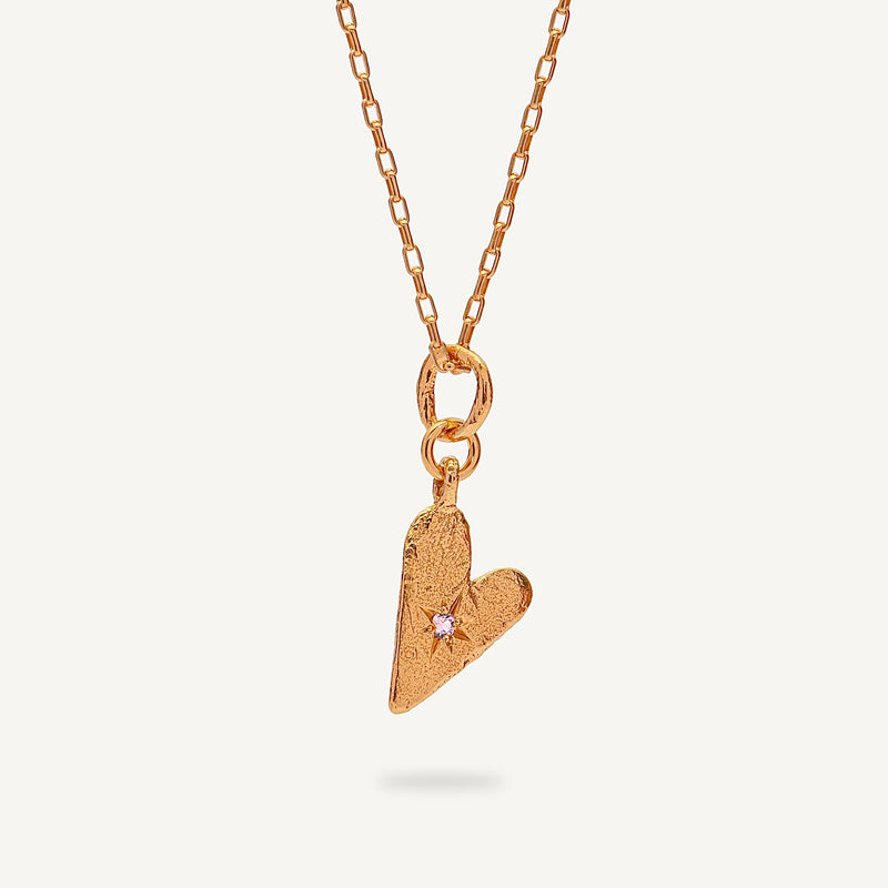 Gold heart-shaped pendant necklace on a light beige background