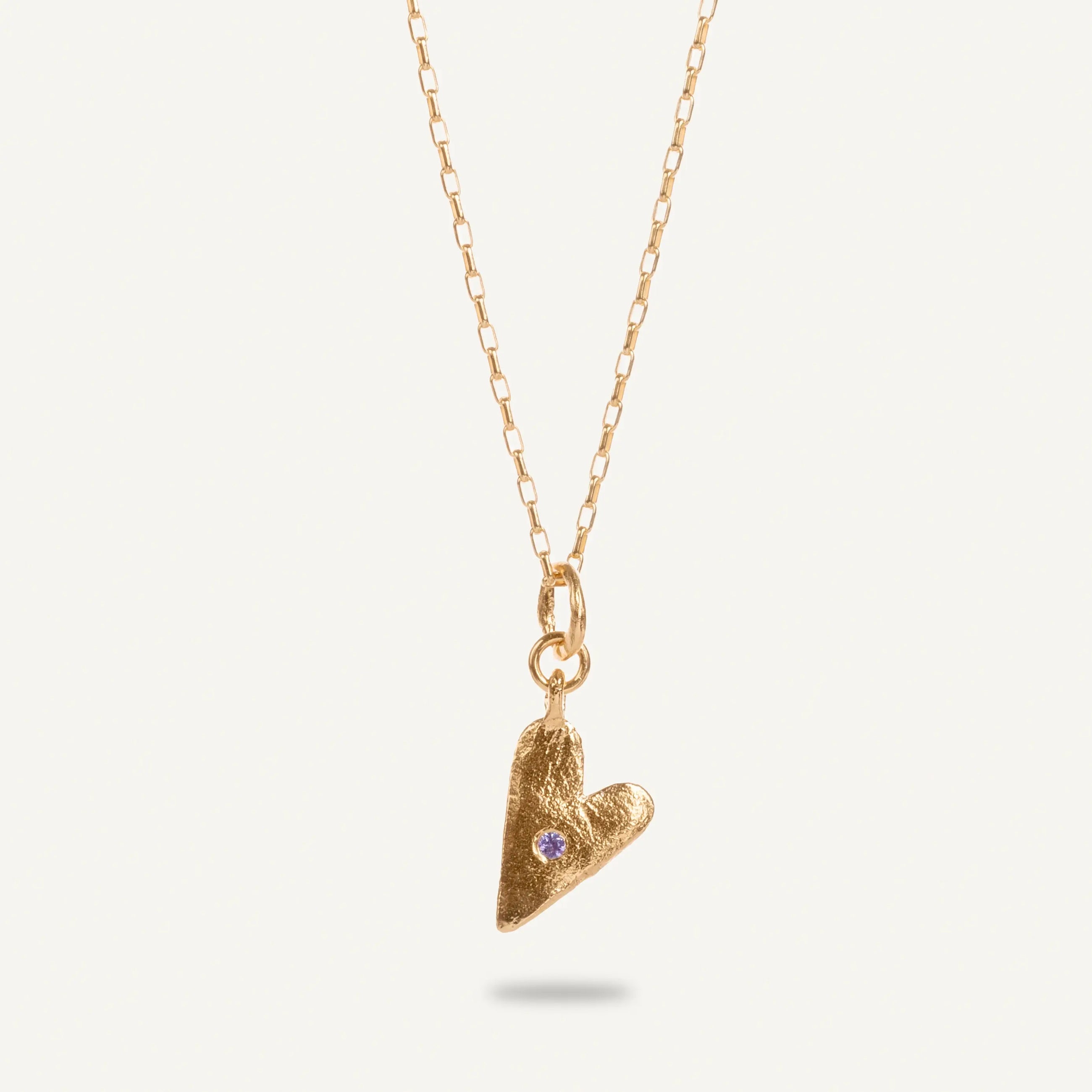 A gold plated silver necklace with a heart-shaped pendant featuring a pink sapphire, displayed against a white background.