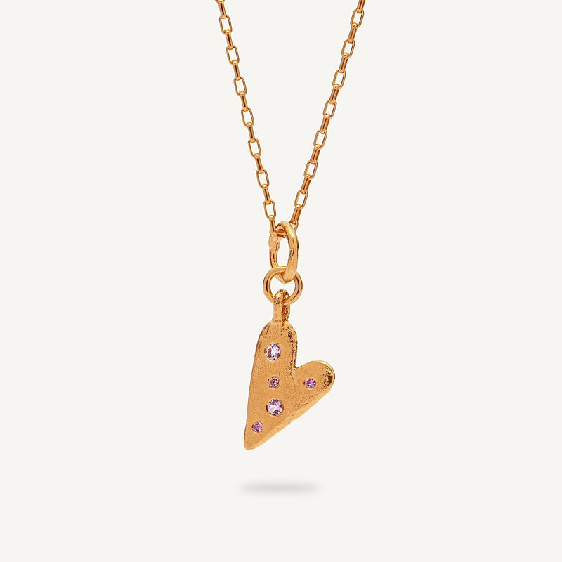Gold heart-shaped pendant necklace with pink gemstones on a light beige background