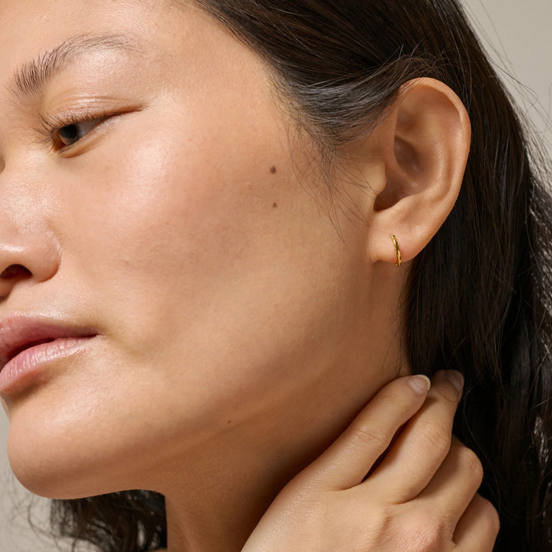 Close-up of a woman wearing a gold earring with a neutral background
