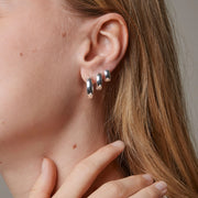 Close-up of a person wearing three silver hoop earrings.
