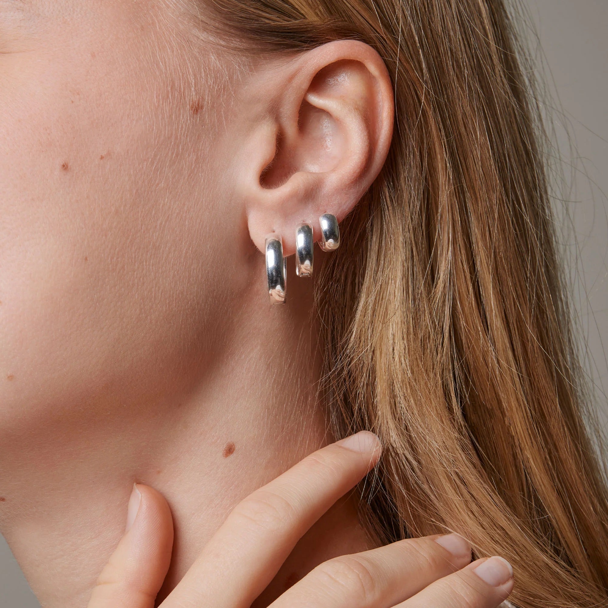 Close-up of a person wearing three silver hoop earrings.