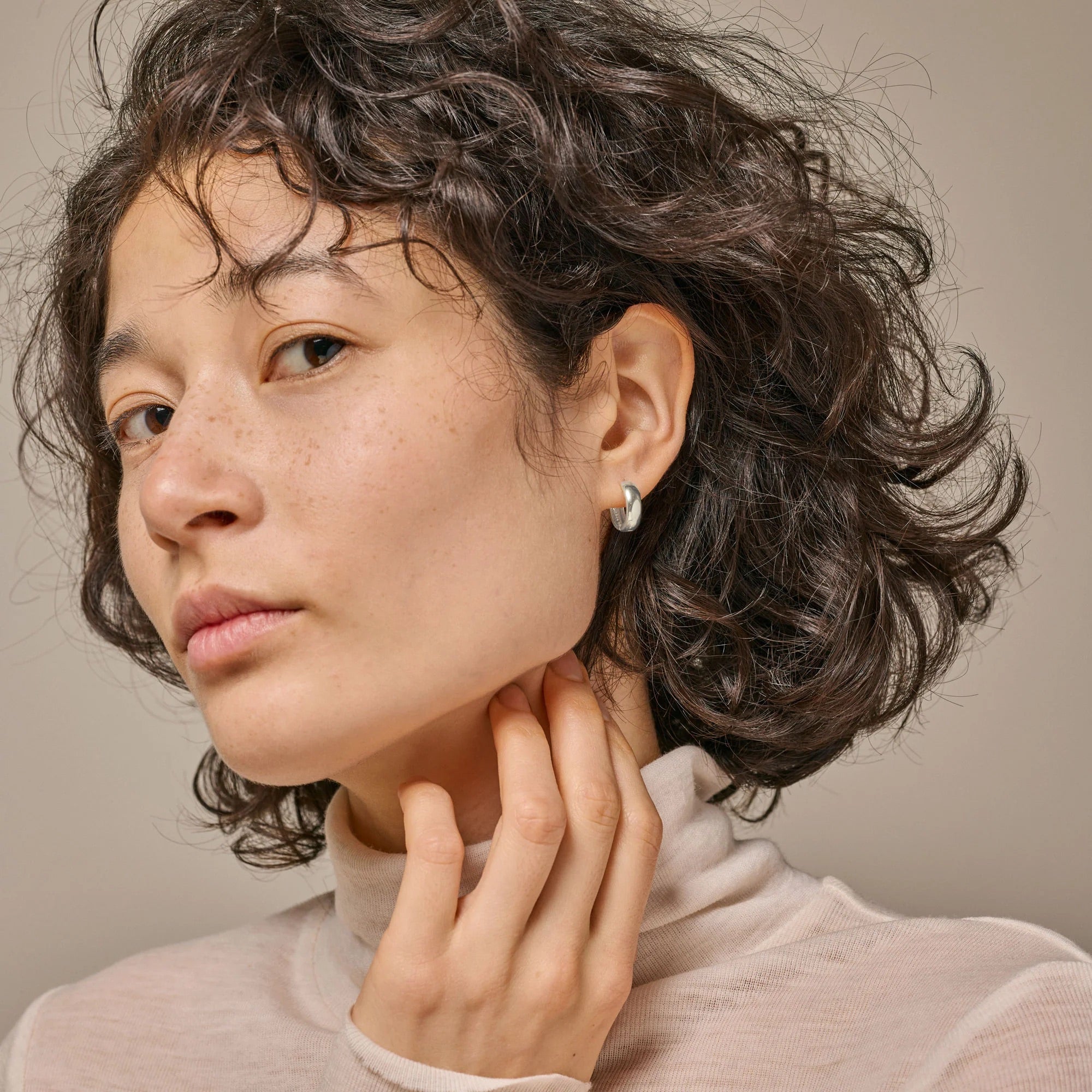 Woman with short curly hair wearing a light-colored turtleneck against a neutral background