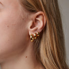 Close-up of a person wearing gold hoop earrings with a neutral background