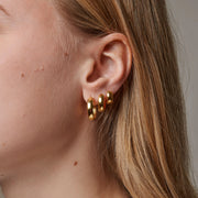 Close-up of a person wearing gold hoop earrings with a neutral background