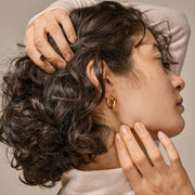 Close-up of a person with styled hair and gold earrings, with hands gently touching the hair and face.