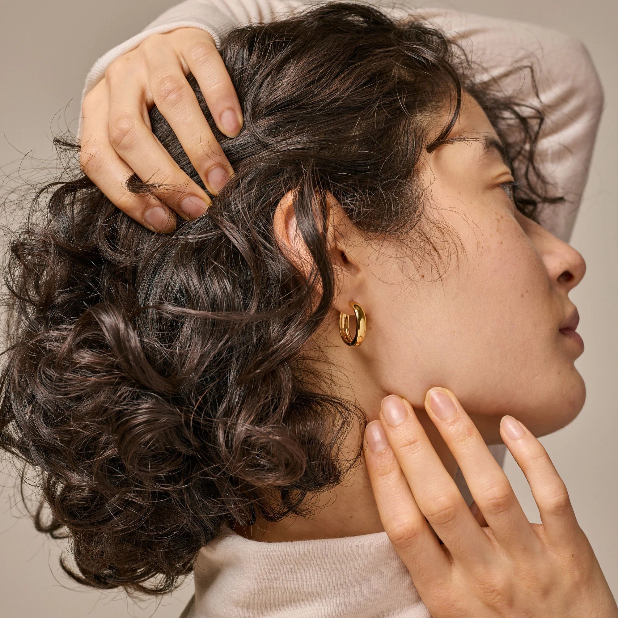 Close-up of a person with styled hair and gold earrings, with hands gently touching the hair and face.