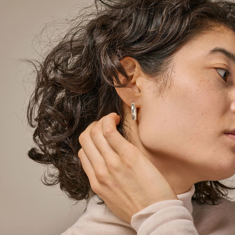 Close-up of a person wearing a silver earring with a neutral background