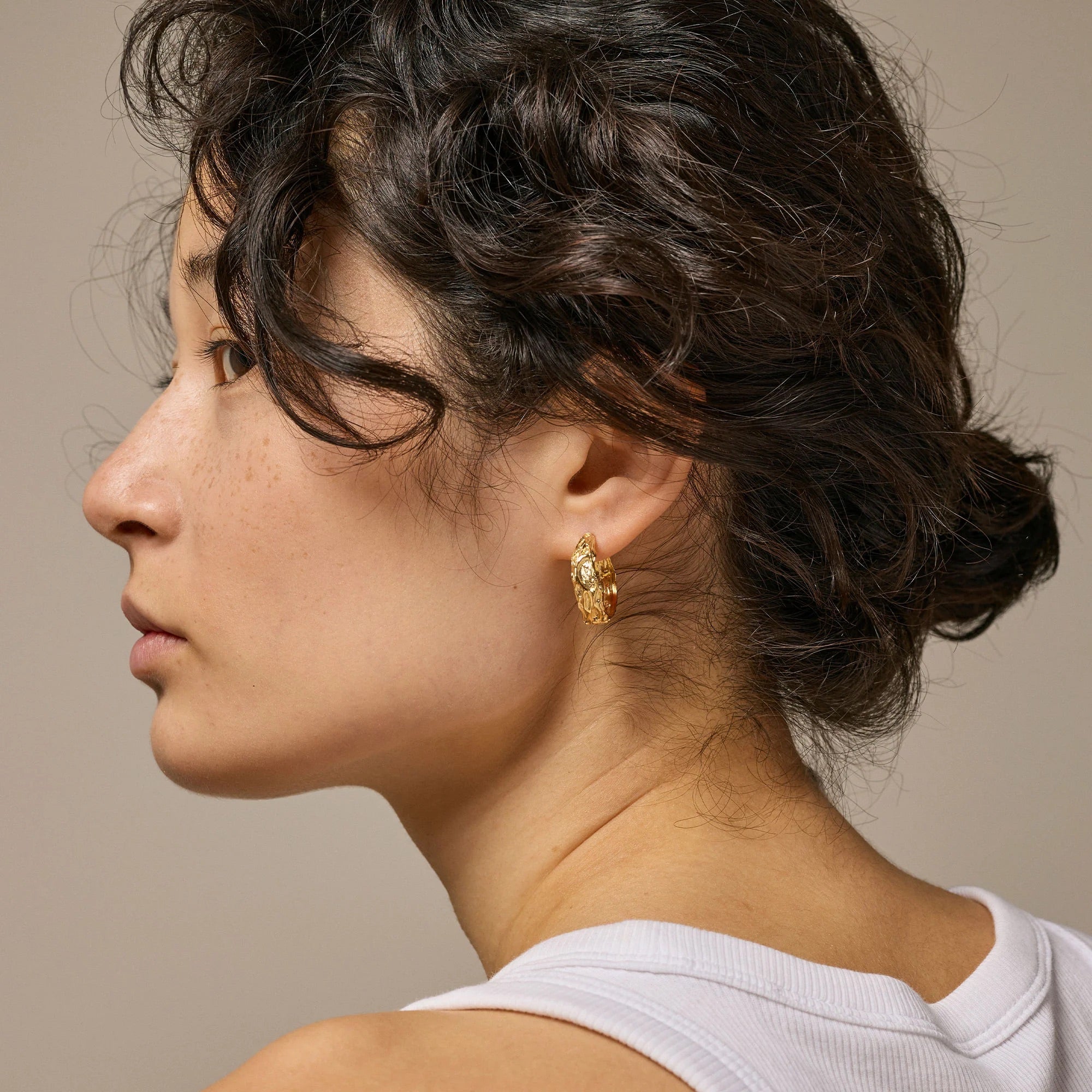 Close-up of a woman wearing gold hoop earrings against a neutral background