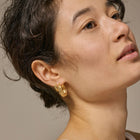 Close-up of a person wearing gold earrings with a neutral background