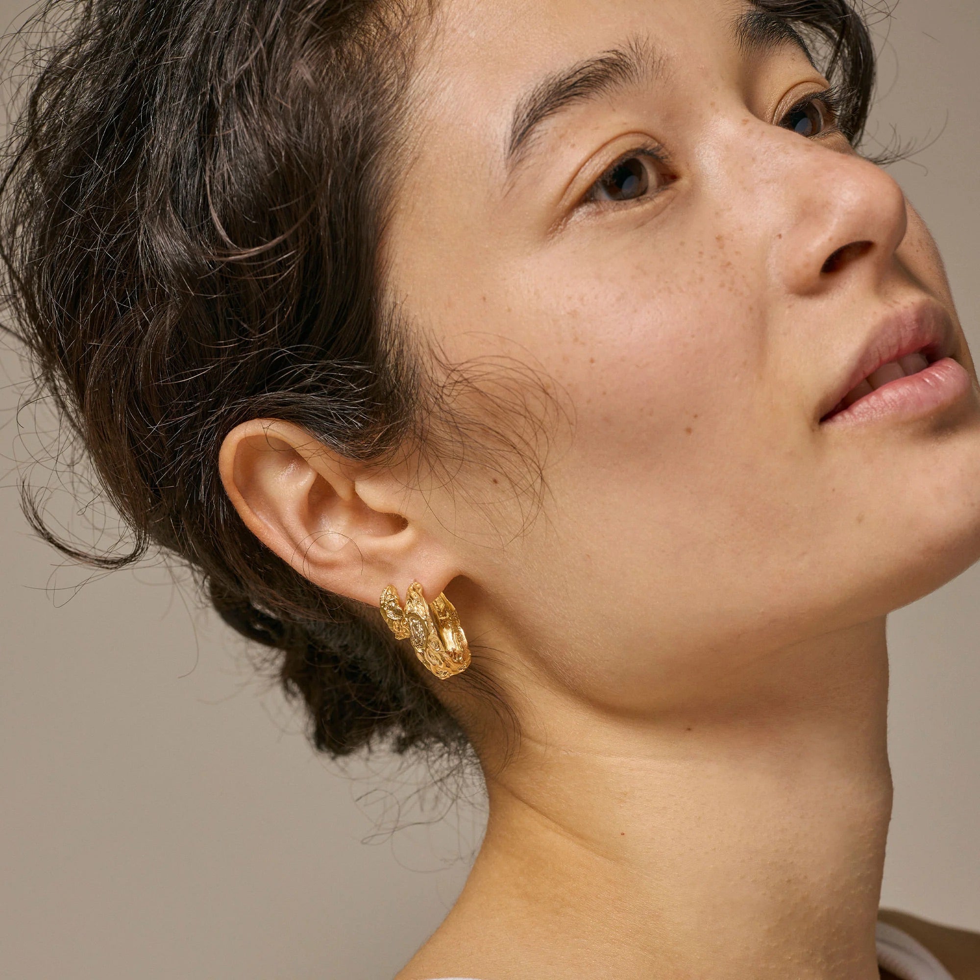 Close-up of a person wearing gold earrings with a neutral background