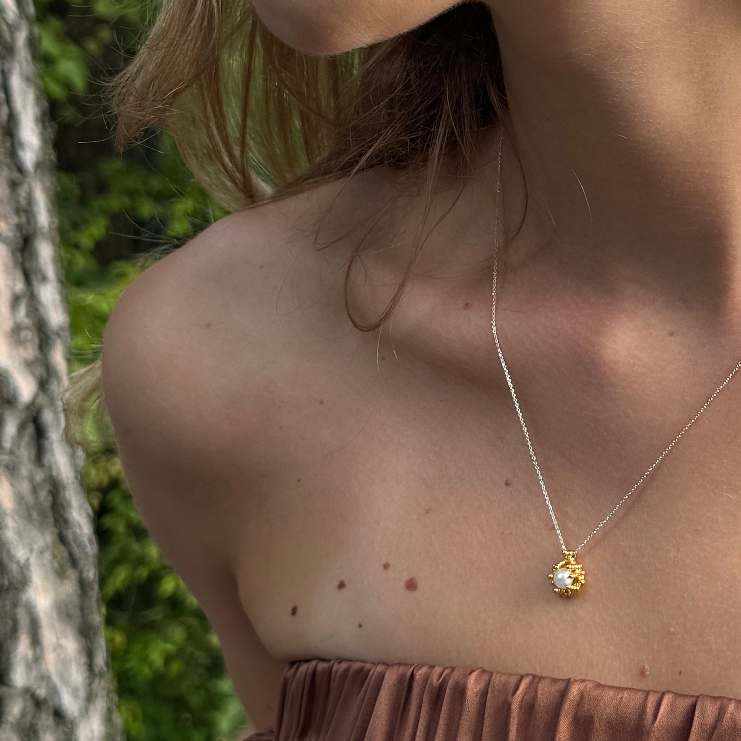 Close-up of a person wearing a gold-plated silver necklace with Akoya pearl