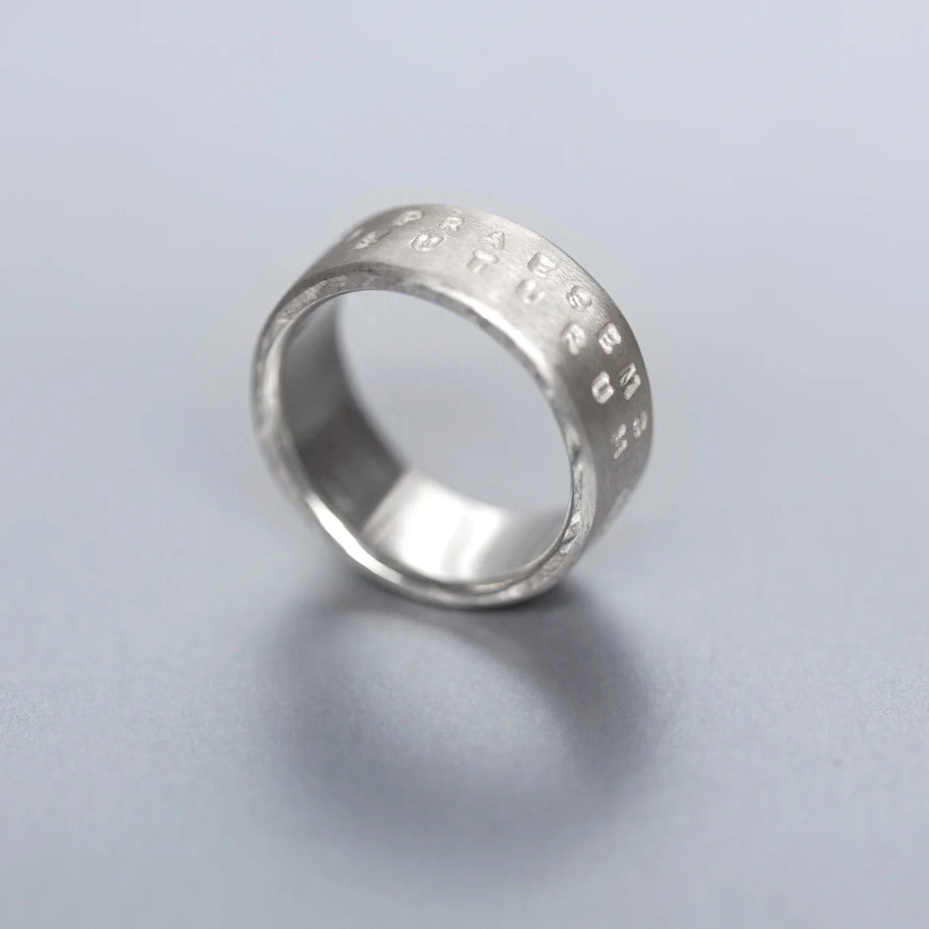 Silver ring with engraved text on a light gray background
