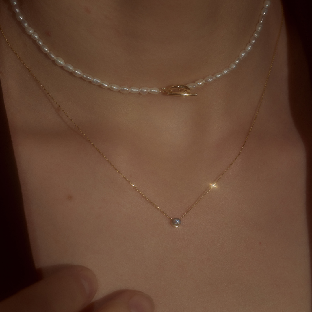 Woman wearing yellow gold & brilliant-cut diamond necklace and pearl necklace.