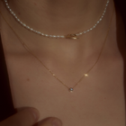 Woman wearing yellow gold & brilliant-cut diamond necklace and pearl necklace.