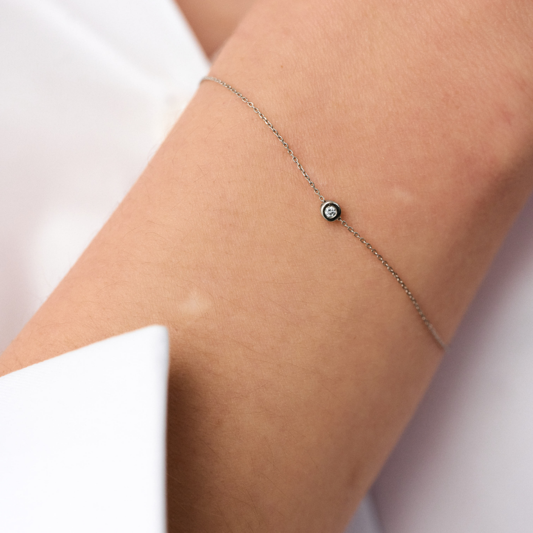 Hand wearing a white gold bracelet featuring a small pendant set with round brilliant-cut diamond.