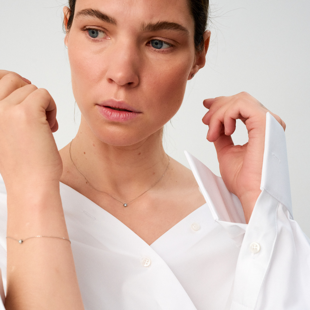 Woman wearing a white gold bracelet featuring a small pendant set with round brilliant-cut diamond.