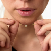 Woman holding yellow gold pendant featuring a round brilliant-cut diamond, suspended from a delicate gold chain. 
